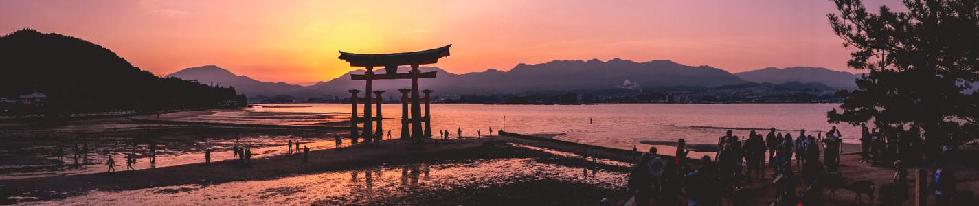 Amazing super wide panorama view of torii gate and sunset with travelers over the sea with mountains in the horizon from the Miyajima Island
