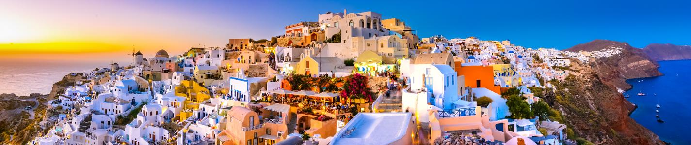 Oia town, Santorini island, Greece: Panoramic view at the sunset. Traditional and famous white houses and churches  with blue domes over the Caldera, Aegean sea.