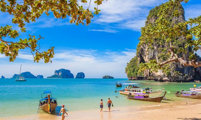 Tropical turquoise water with a Thai longtail boat motoring past a coral reef and Ko Poda Island in the Andaman sea of Krabi Thailand