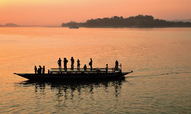 Silhouette of people sailing in a boat over river Brahmaputra during sunset