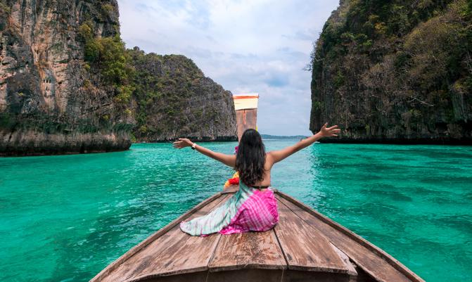 happy Asian woman traveler sit on a long-tailed boat looking at beautiful natural Pileh lagoon Krabi in Phi Phi Island. sea travel Phuket Thailand, Tourist girl relax on summer vacation.