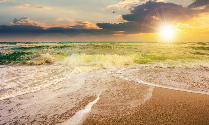 sea tide on a cloudy sunrise. green waves crashing golden sandy beach in morning light. storm weather approaching. summer holiday concept.